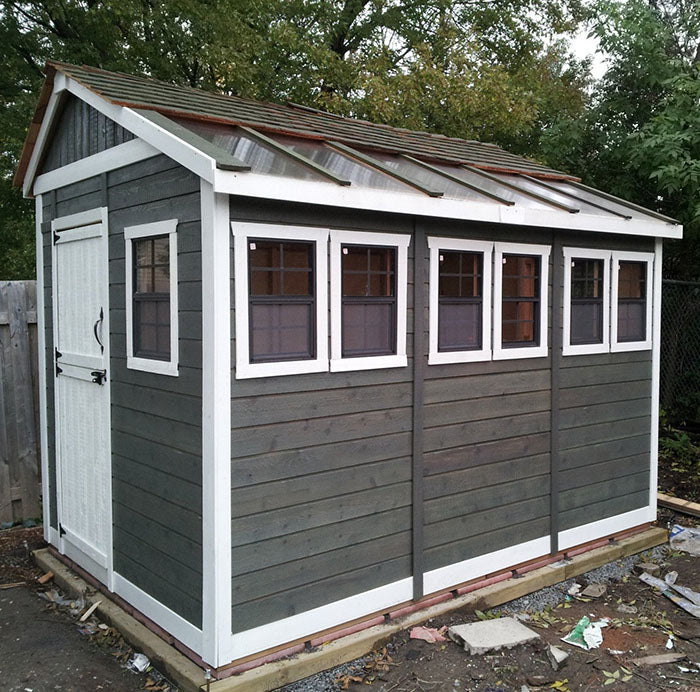 Two-tone black and white Outdoor Living Today Sunshed Garden Shed, 8x12, with multiple windows and rustic charm, set against a natural backdrop.